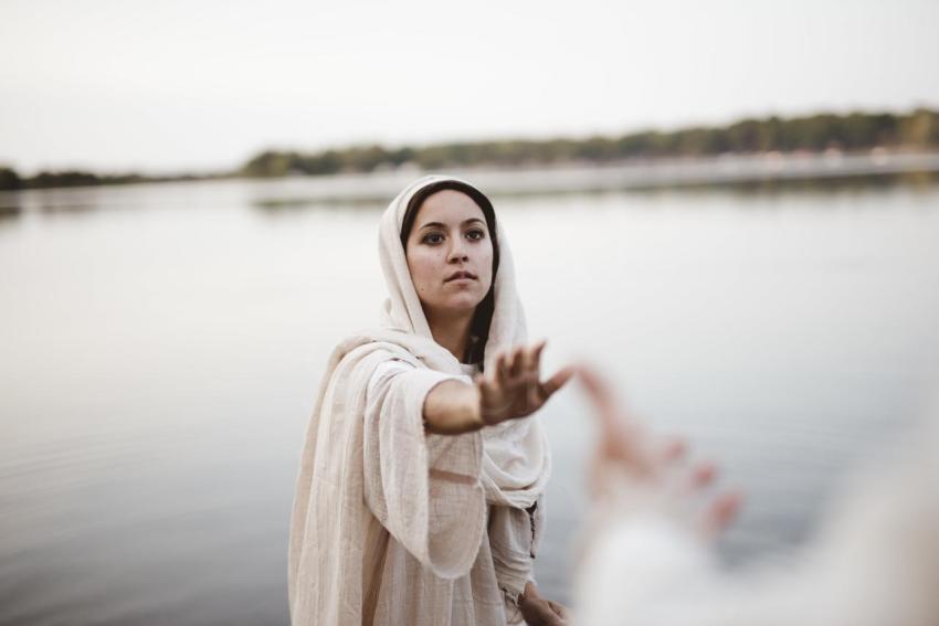 Shallow focus shot of a female wearing a biblical robe while reaching towards hand of Jesus Christ