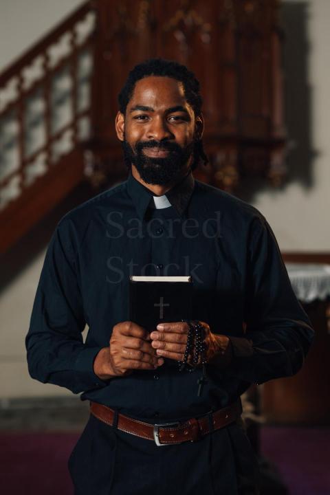 Young priest smiling and holding bible in church